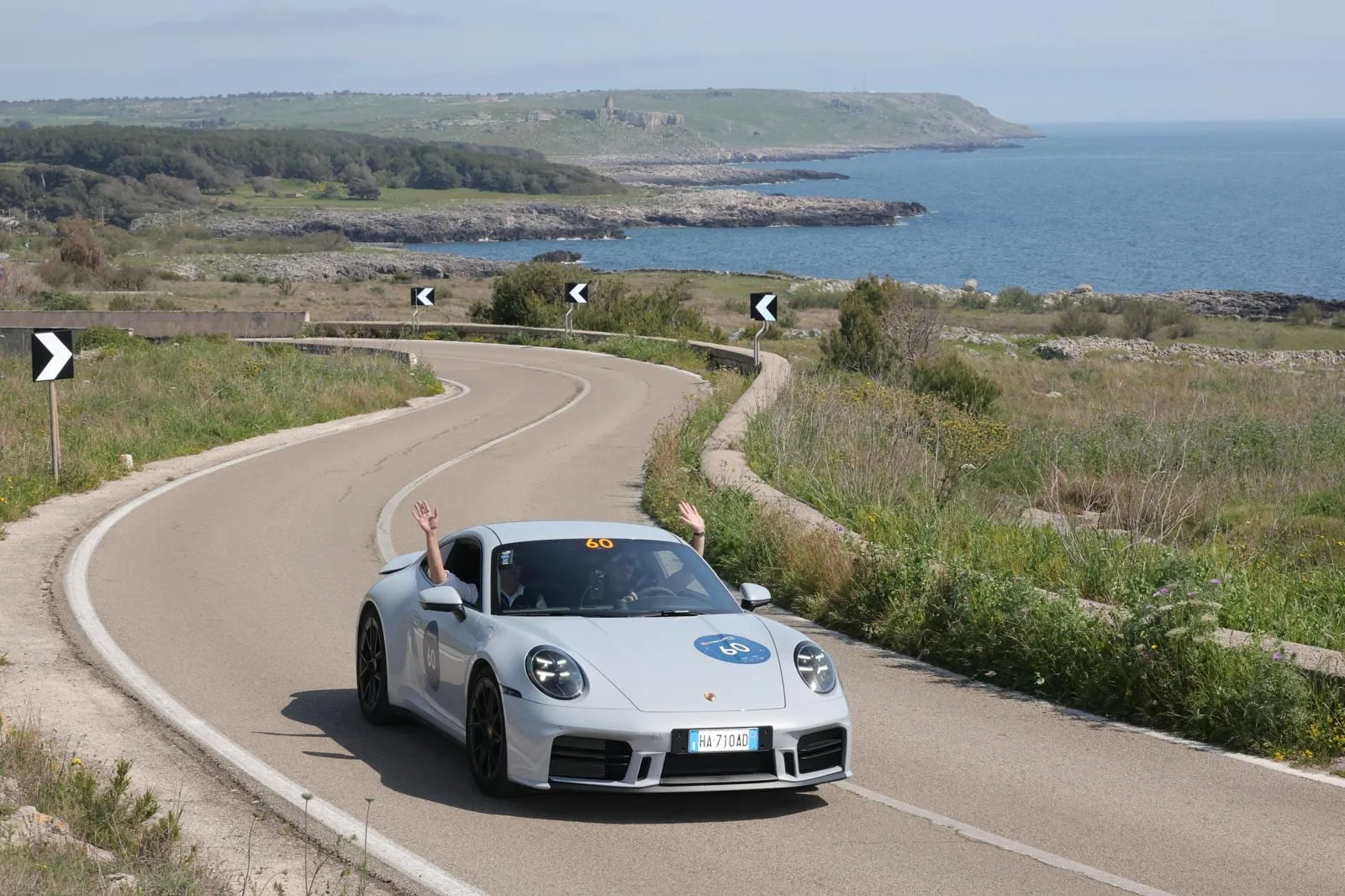 L’auto 60, una Porsche 911 argento del 2025, su una strada costiera sopra il mare in Puglia