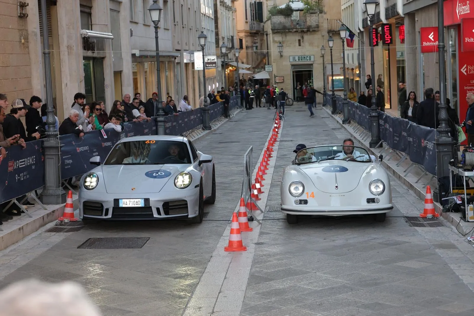 L’auto 60, una Porsche 911 argento del 2025, accanto a una Porsche 356 Speedster bianca in una prova cronometrata tra i coni in una via di Lecce, con il pubblico dietro le transenne